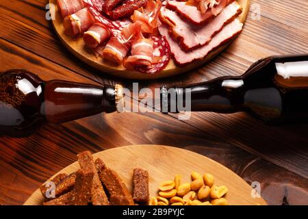 Zwei Flaschen Bier und verschiedene Snacks für jeden Geschmack auf Holzgrund. Fleischprodukte, Wurstscheiben, Pommes, Nüsse, Croutons. Stockfoto