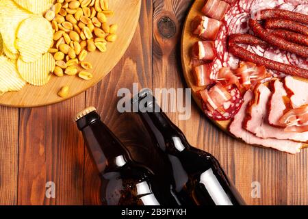Zwei Flaschen Bier und verschiedene Snacks für jeden Geschmack auf Holzgrund. Fleischprodukte, Wurstscheiben, Pommes, Nüsse, Croutons. Stockfoto