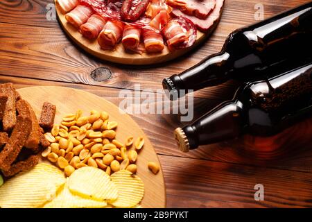 Zwei Flaschen Bier und verschiedene Snacks für jeden Geschmack auf Holzgrund. Fleischprodukte, Wurstscheiben, Pommes, Nüsse, Croutons. Stockfoto