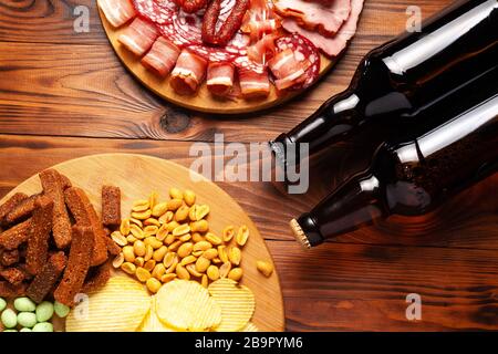 Zwei Flaschen Bier und verschiedene Snacks für jeden Geschmack auf Holzgrund. Fleischprodukte, Wurstscheiben, Pommes, Nüsse, Croutons. Stockfoto