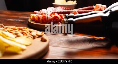 Zwei Flaschen Bier und verschiedene Snacks für jeden Geschmack auf Holzgrund. Fleischprodukte, Wurstscheiben, Pommes, Nüsse, Croutons. Stockfoto