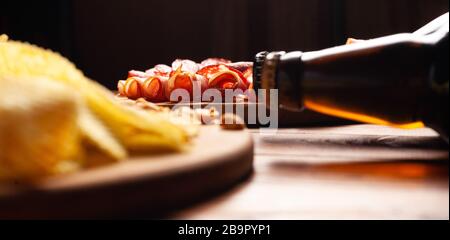 Zwei Flaschen Bier und verschiedene Snacks für jeden Geschmack auf Holzgrund. Fleischprodukte, Wurstscheiben, Pommes, Nüsse, Croutons. Stockfoto