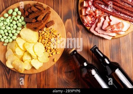 Zwei Flaschen Bier und verschiedene Snacks für jeden Geschmack auf Holzgrund. Fleischprodukte, Wurstscheiben, Pommes, Nüsse, Croutons. Stockfoto