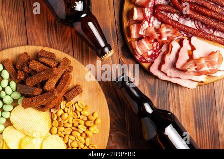Zwei Flaschen Bier und verschiedene Snacks für jeden Geschmack auf Holzgrund. Fleischprodukte, Wurstscheiben, Pommes, Nüsse, Croutons. Stockfoto