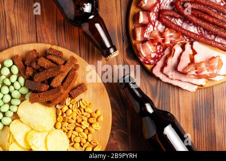 Zwei Flaschen Bier und verschiedene Snacks für jeden Geschmack auf Holzgrund. Fleischprodukte, Wurstscheiben, Pommes, Nüsse, Croutons. Stockfoto