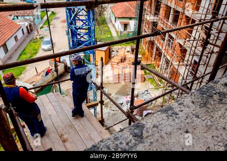 Rigger stehen auf Gerüst mit hölzernen Plattform hoch oben auf dem Gerüst über Baustelle. Stockfoto