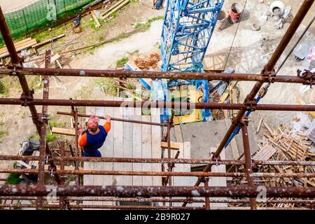 Das Gerüst wird gegen das Gebäude gestellt. Chef wird von der Holzplattform über der Baustelle beaufsichtigt. Stockfoto