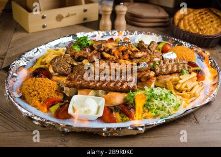 Volle Sicht auf den Persischen Mix Kebab von Hackfleisch und Hühnchen mit Reis und Pommes frites und Gemüse in einem großen traditionellen Fach auf hölzernen Tisch Stockfoto