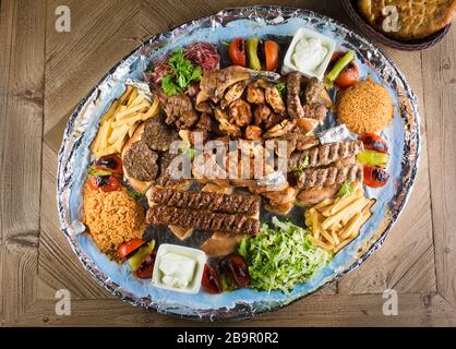 Volle Sicht auf den Persischen Mix Kebab von Hackfleisch und Hühnchen mit Reis und Pommes frites und Gemüse in einem großen traditionellen Fach auf hölzernen Tisch Stockfoto