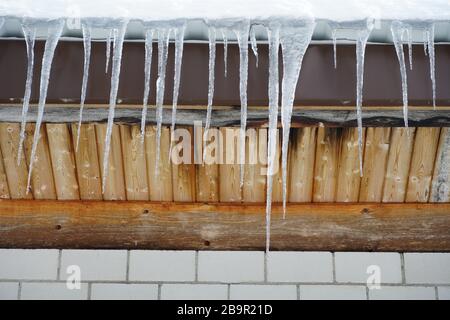 Eine lange Reihe schmelzender Eiszapfen hängt vom Holzdach und kündigt das Ende des Winters und den kommenden Frühling oder das Tauwetter als Symbol an Stockfoto