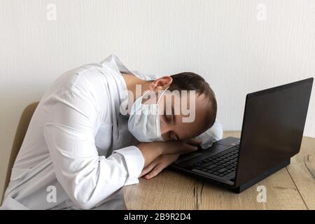 Junger Arzt in Maske schläft auf dem Schreibtisch ein Stockfoto