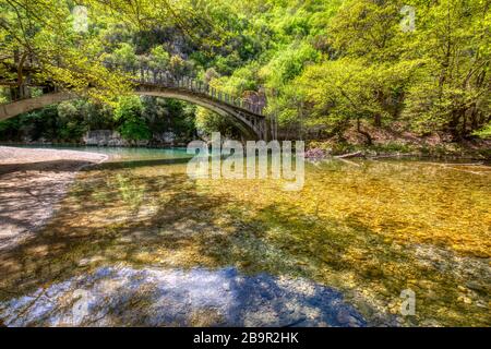 Brücke über den Fluss Voidomatis unter grünen gelben, sonnigen Bäumen in der Region Zagori, Epirus, Griechenland Stockfoto