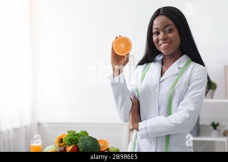 Positive schwarze Frau Ernährungsberaterin hält orangefarbene Hälfte Stockfoto