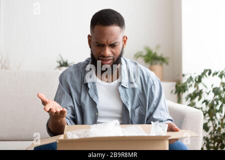 Lieferfehler beim Kauf. Überraschter Mann öffnete das Paket Stockfoto