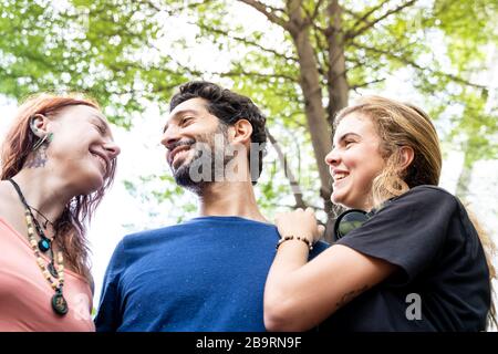 Zwei junge Frauen umarmen einen Jungen unter einem Baum auf der Straße Stockfoto