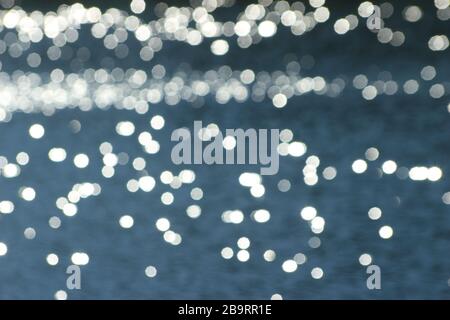 Das unscharfe Hintergrundbild ist eine türkisfarbene Wasseroberfläche und die Wasseroberfläche reflektiert die glitzernde Sonne. Stockfoto