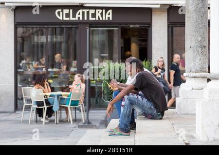 CREMES, ITALIEN - 2. SEPTEMBER 2015: Zwei schwarze Männer sitzen mit einem Telefon in den Händen auf den Stufen des Gebäudes. Cremona. Italien Stockfoto