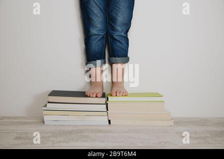 Kind steht auf Stapel von Büchern. Weltbuch-Tageskonzept Stockfoto