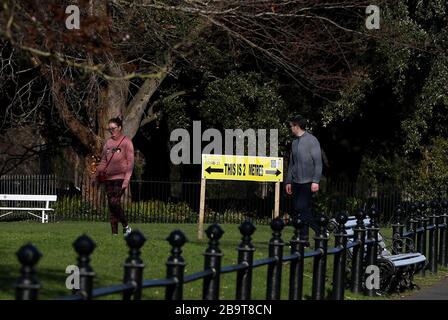 Die Menschen gehen an einem Zeichen vorbei, das die soziale Distanzierung im Phoenix Park von Dublin fördert, da Taoiseach Leo Varadkar eine Reihe von umfassenden Maßnahmen zur Bekämpfung des Coronavirus eingeführt hat, einschließlich der Einschränkung aller öffentlichen Versammlungen auf vier Personen. Stockfoto