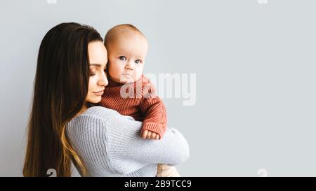 Glückliche Mutter, die ihr Baby hochhält. Junge schöne Mutter hält ihr Baby und ihre Kuscheltiere, Mutterschaft Konzept Stockfoto