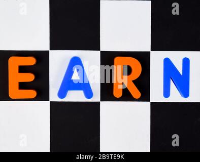 Verdienen Sie ein Wort, das mit verschiedenen farbigen Buchstabenblocks geschrieben wurde, die auf einem schwarz-weißen Hintergrund angeordnet sind Stockfoto