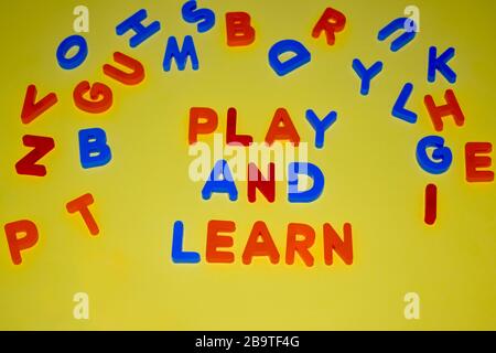 Spielen und lernen Sie Wörter, die mit verschiedenen farbigen Buchstabenblocks geschrieben wurden, die auf einem gelben Hintergrund verstreut sind Stockfoto