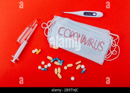 Medizinische Schutzmaske mit der Aufschrift Coronavirus, Spritzen, Ampullen, Thermometer und Medikamente auf rotem Grund. Schutzmaske als Vorsichtsmaßnahme. Stockfoto