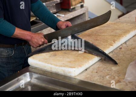 FUNCHAL, PORTUGAL - 15. FEBRUAR 2020: Unidentifizierter Mann schneidet Haifischschwanz bei Mercado dos Lavradores (Bauernmarkt) in Funchal auf der Insel Madeira, Po Stockfoto