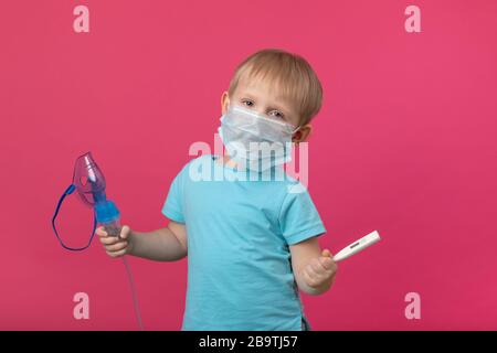 Ein blondes Kind mit Inhalator und Thermometer in der Hand auf einem einfarbig rosafarbenen Hintergrund. Studio-Fotografie zur Behandlung von Temperatur, Husten und Stockfoto
