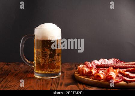 Becher mit Bier und einer Auswahl an Snacks auf einem Holztisch. Wurst, Salami, Schinken, Speck. Bier salzig Snack, Pommes, Wasabi Nüsse, gesalzene Erdnüsse, Croutons. Stockfoto