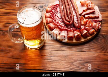 Becher mit Bier und einer Auswahl an Snacks auf einem Holztisch. Wurst, Salami, Schinken, Speck. Bier salzig Snack, Pommes, Wasabi Nüsse, gesalzene Erdnüsse, Croutons. Stockfoto