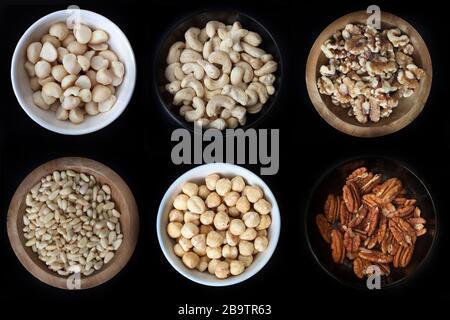 6 kleine Nussschüsseln: Macadamias, Cashews, Walnüsse, Kiefernnüsse, Haselnüsse und Pekannüsse Stockfoto