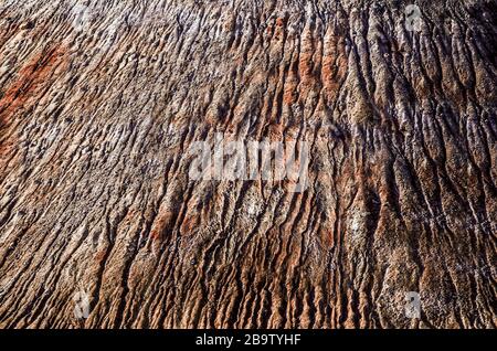 Abstrakte Geländestruktur auf einem Hügel, der mit Sand und kleinen Steinen und ineinander verschlossener Lehmmasse bestreut ist Stockfoto