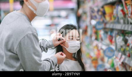 Mutter, die eine Schutzmaske trägt, legt eine Gesichtsmaske auf eine Tochter im Supermarkt. Sicherheit bei COVID-19-Ausbruch. Epidemie des Viruskovids, Stockfoto