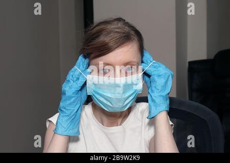 Junge Frau, die mit medizinischen Handschuhen die Maske des Chirurgen auf ihr Gesicht legt Stockfoto