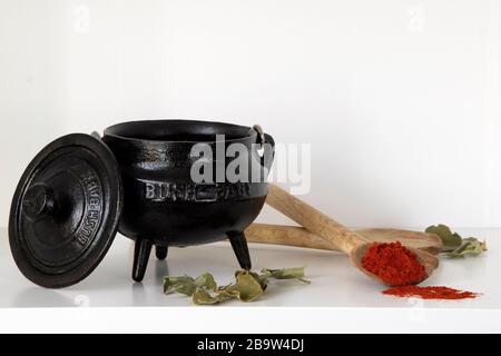 Dreibeiniger schwarzer Topf, Holzlöffel und Paprika auf weißem Regal Stockfoto