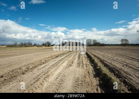 Sandige Straße durch gepflügte Felder, weiße Wolken am blauen Himmel, Blick auf den Frühling Stockfoto