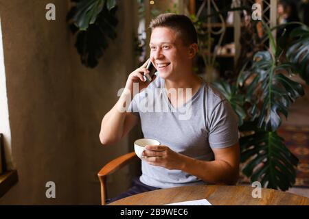 Junger Mann, der mit dem Smartphone spricht und Kaffee im Café trinkt. Stockfoto