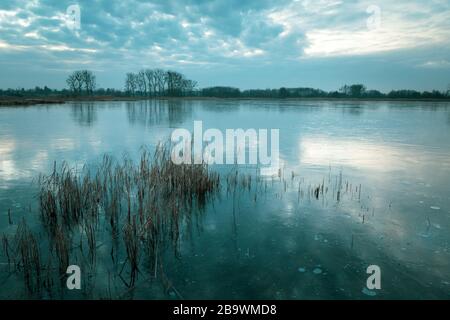 Im gefrorenen See, am Horizont Bäume und am Himmel Wolken Stockfoto