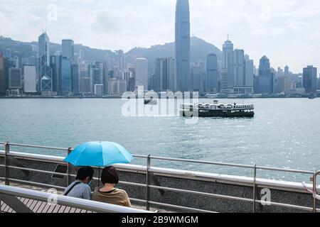 Hongkong, China. März 2020. Ein Paar mit einem Regenschirm sitzt am Victoria Harbour in Hongkong. Weltweit wurden mehr als 420.000 Menschen mit dem neuen Coronavirus infiziert, und die Zahl der Todesfälle durch den Ausbruch nimmt weiter zu. Kredit: Keith Tsuji/ZUMA Wire/Alamy Live News Stockfoto