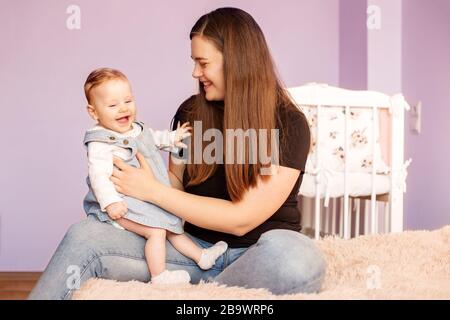 Mutter spielt mit ihrer neugeborenen Tochter im Zimmer. Das Konzept der Familie, der Mutterschaft und der Kinderbetreuung. Stockfoto