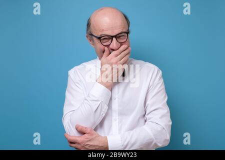 Älterer Mann lachend und peinlich kichernd, den Mund mit den Händen bedeckend Stockfoto