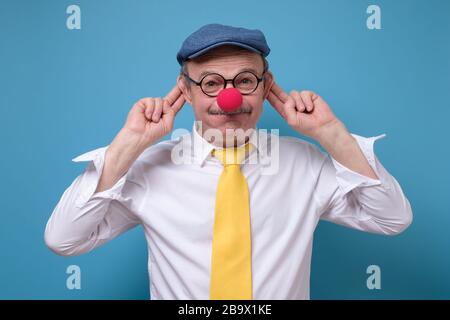 Älterer kaukasischer Mann mit roter Nase, Hut und Brille, die grimazing. Stockfoto