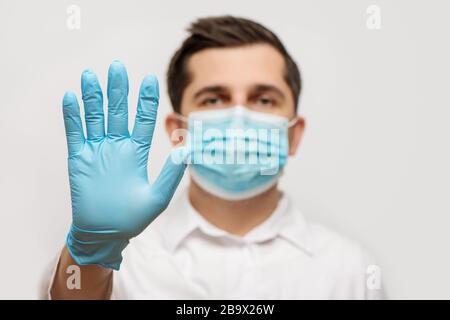 Porträt des Arztes in medizinischer Uniform mit blauer Gesichtsmaske und einer Handschuhhand, die ein Stoppschild zeigt. COVID-19-Konzept beenden. Stockfoto