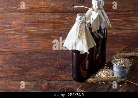 Hausgemachtes dunkles Bier in Flaschen und ein Glas auf dunklem Hintergrund. In der Nähe liegen Gerstenkörner und Weizenkörner. Dunkler Hintergrund. Kopierbereich Stockfoto