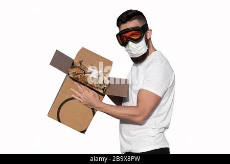 Mann mit Schutzbrille und Gesichtsmaske Auspacken von Pappkarton auf weißem Hintergrund. Kontaktlose Lieferung während der Pandemie des Coronavirus Covid-19-Konzepts Stockfoto