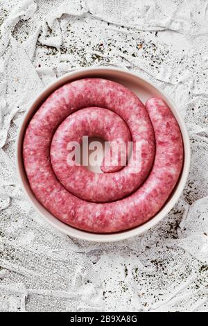 Hochwinkeliger Blick auf eine gerollte Botifarra, eine für Katalonien typische Schweinefleischwurst in Spanien, auf einem Teller, auf einem weißen texturierten Textilhintergrund Stockfoto