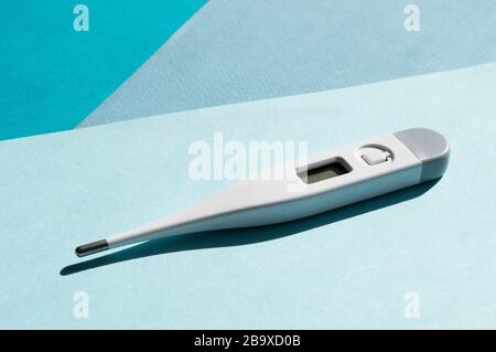 Ein elektronisches Kunststoffthermometer mit Schatten, isoliert auf sonnigem hellblauem und türkisfarbenem Hintergrund. Konzept für die Behandlung von Gesundheitsleistungen Stockfoto