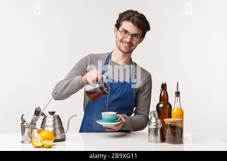 Barista, Café-Mitarbeiter und Barkeeper Konzept. Portrait des freundlichen lächelnden netten Angestellten, der Filterkaffee vom Wasserkocher zur Tasse gießt und schaut Stockfoto