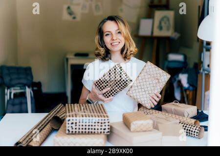 Eine junge Frau hält eingepackte Geschenke und lächelt charmant. Stockfoto